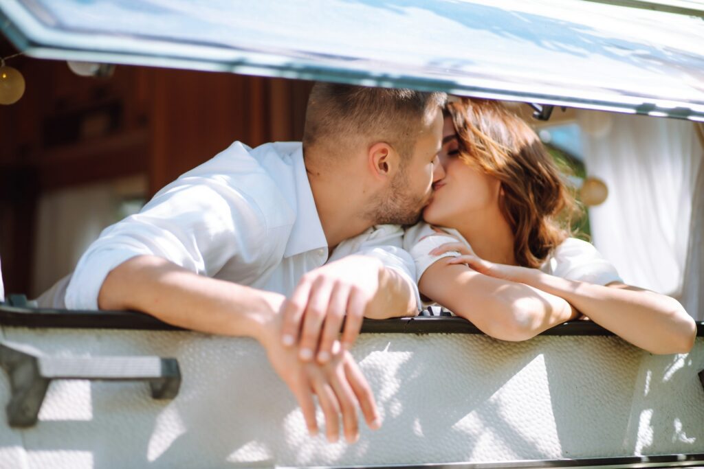 Beautiful wedding couple laugh and kiss relaxing in rv, camping in a trailer. Romantic moment.